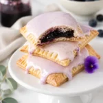 Homemade blueberry Pop Tarts stacked on a white cake stand with pale icing and thick blueberry filling