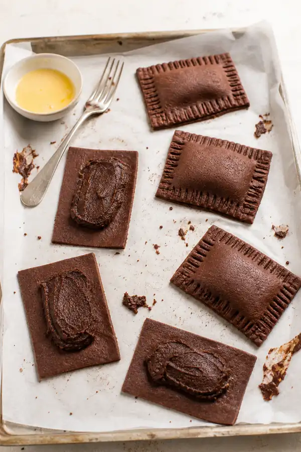 Homemade chocolate fudge pop tarts being assembled with thick fudge filling, clean pastry borders, egg wash, and crimped edges