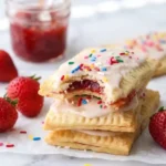 Homemade strawberry pop tarts stacked with strawberry jam filling, pink glaze, and sprinkles