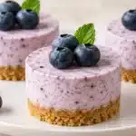 No-Bake Blueberry Mini Cheesecakes with pale lavender filling, graham crusts, blueberries, and mint
