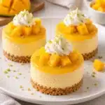 No-Bake Mango Mini Cheesecakes in clear paper-lined muffin wells with vanilla crumbs, creamy mango filling, and diced mango
