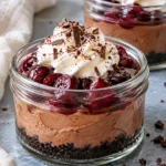Black forest cheesecake jars with chocolate crumbs, cocoa cheesecake, cherries, whipped cream and chocolate shavings